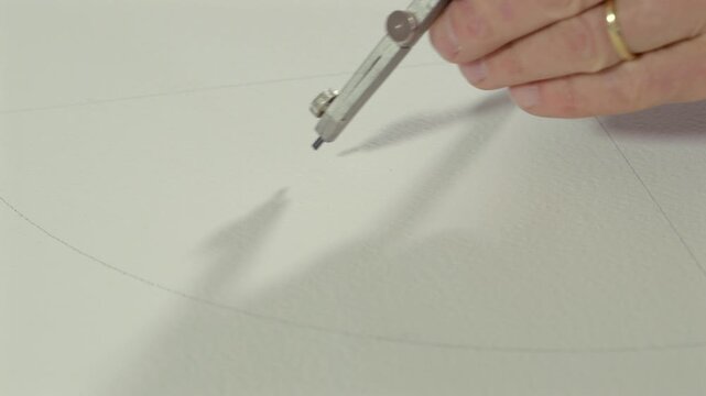 Close-up of a hand using a metal compass to draw a circular arc on white paper. Concept of geometry, precision, technical drawing, architecture and creative design.