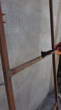 Close up hand with paintbrush coating rusty metal frame profiles