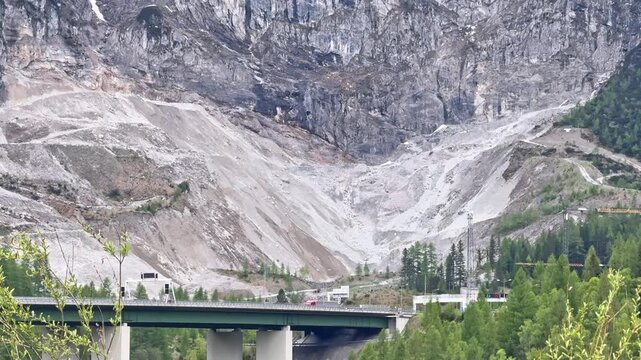 Austrian alpine highway bridge near Flachau crosses a forested valley below rugged snow-covered mountains and steep rocky slopes.