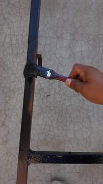 Manual brush painting over severely rusty cylindrical iron pipe structure