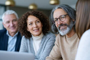 Fototapeta premium Three smiling adults gather around a laptop. Their expressions convey warmth and engagement. The scene suggests collaborative learning or group discussion