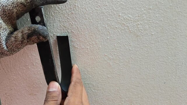 Worker aligning and positioning iron flat bar base against concrete wall