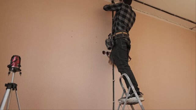 Electrician standing on a ladder installing new electrical wiring in an apartment using a screwdriver professional electrical system installation during home renovation