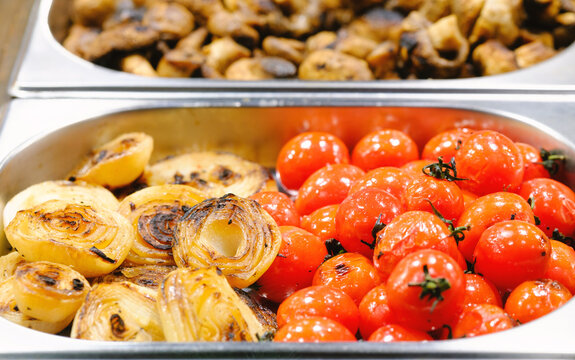 Warm grilled onions and roasted red cherry tomatoes displayed in metallic buffet trays catering food service.