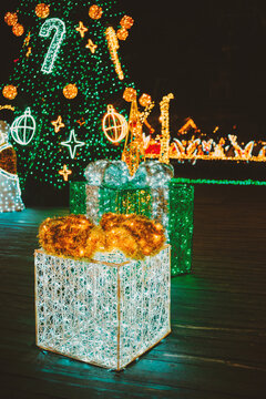 Bright green Christmas tree with sparkling golden lights and two glowing holiday gift boxes at night