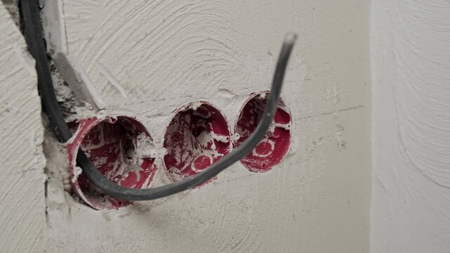 Detail shot as camera moves toward installed junction boxes in concrete wall. New electrical wiring installation and fixation during construction stage.