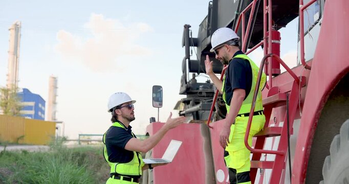 Adult Caucasian male logistics supervisor on truck step explains route update to colleague using laptop, managing container dispatch, inspection workflow, safety rule, freight decision at yard