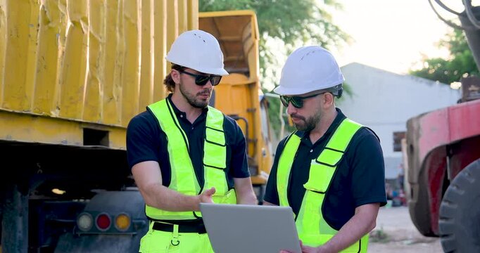 Adult Caucasian male logistics crew operate laptop under yellow container trailer, verifying cargo documentation, inventory record, dispatch schedule, safety compliance, shipment tracking near truck