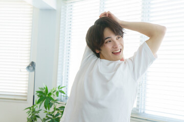 Fototapeta premium 窓際でストレッチをする笑顔の若い日本人男性