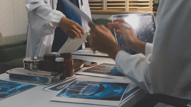 Medical professionals working together at an office desk, discussing information on a laptop, a male doctor pointing at the screen while holding a digital tablet