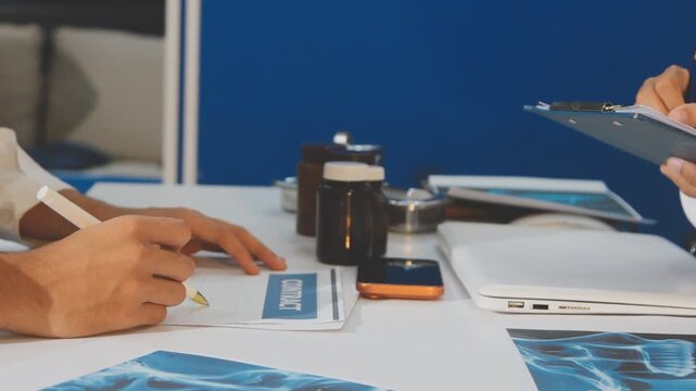 Medical professionals working together at an office desk, discussing information on a laptop, a male doctor pointing at the screen while holding a digital tablet