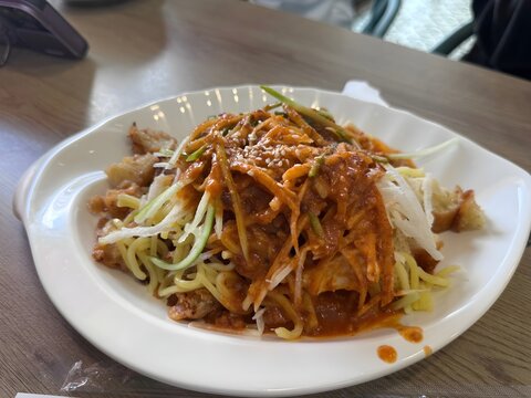 A plate of Malaysian rojak mee featuring yellow noodles topped with spicy sauce, shredded cucumber, radish, sesame seeds, and crispy fritter pieces. This popular local street food combines sweet, spic