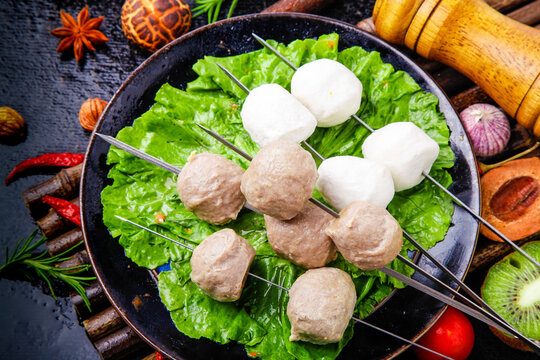 Grilled pork and beef meatball skewers with fresh lettuce and spices on rustic wooden table
