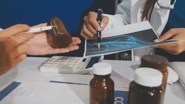 Medical professionals working together at an office desk, discussing information on a laptop, a male doctor pointing at the screen while holding a digital tablet