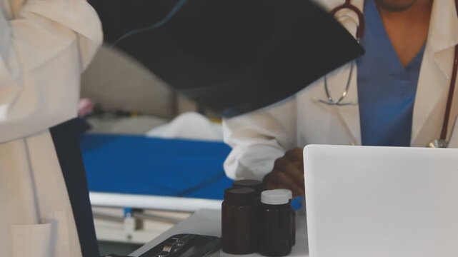 Medical professionals working together at an office desk, discussing information on a laptop, a male doctor pointing at the screen while holding a digital tablet