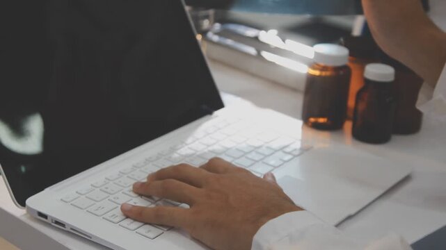 Medical professionals working together at an office desk, discussing information on a laptop, a male doctor pointing at the screen while holding a digital tablet