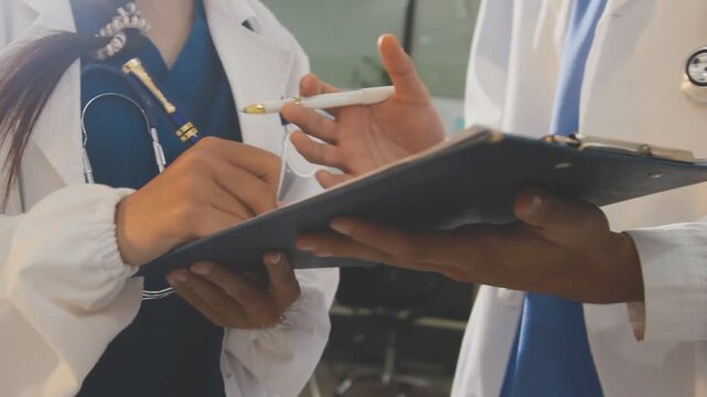 Medical professionals working together at an office desk, discussing information on a laptop, a male doctor pointing at the screen while holding a digital tablet