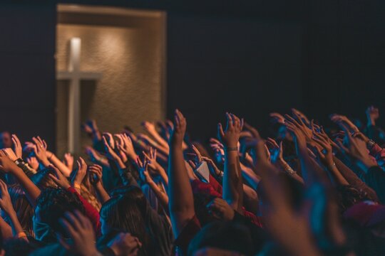 Christian crowd raising hands in worship towards cross during church service