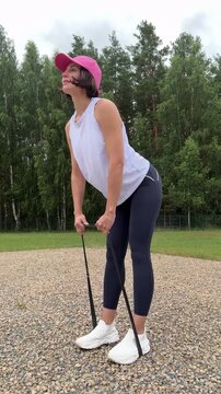 Profile view of an athletic brunette woman performing a resistance band deadlift or hip hinge workout to strengthen her glutes and hamstrings outdoors