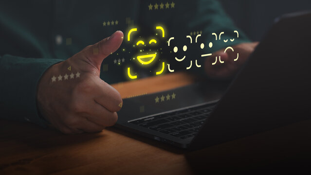 Hand showing thumbs up with laptop and glowing emoji rating hologram. Positive customer review, excellent service satisfaction and digital feedback concept.