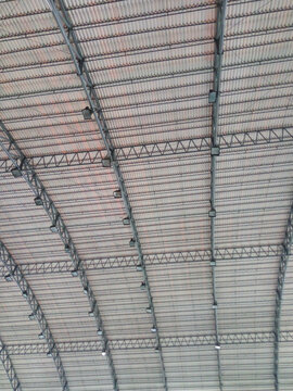 Modern industrial roof structure featuring steel trusses and corrugated metal ceiling inside a large warehouse or factory building. Suitable for architecture, engineering, construction, industrial fac