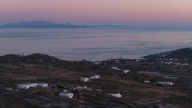 Airplane taking off in Mykonos airport, Aegean Sea with typical whitewashed cycladic architecture with gentle sunset light in Greece