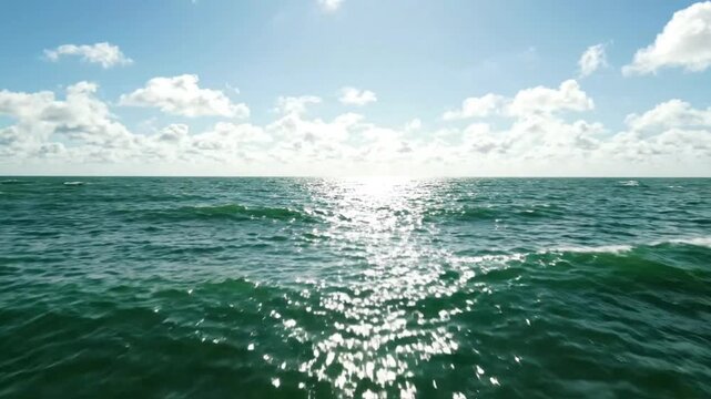 Scenic view of calm green ocean waves under a bright sunny sky with clouds
