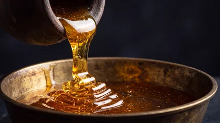 Thick wild honey pouring from clay pot into brass bowl with golden folds macro action © Arif