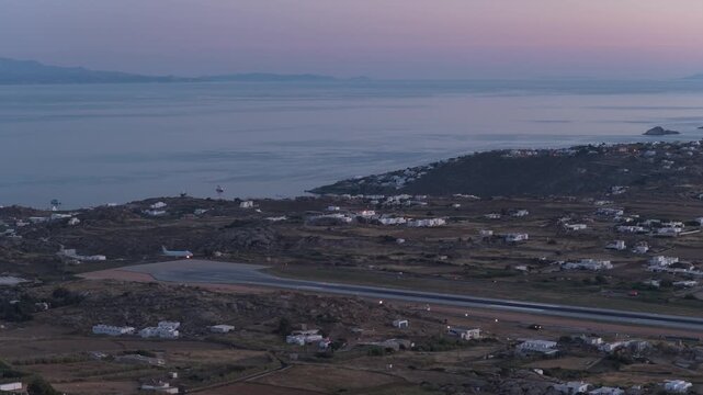 Commercial passenger airplane landing at Mykonos airport runway during summer twilight with the Aegean Sea background, popular tourist vacation destination
