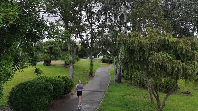 Female runner in activewear burning calories with a cardio workout. Sporty woman jogging running on city park bridge outdoors. Woman exercising with earphones on in the morning. Copy space Stock Photo