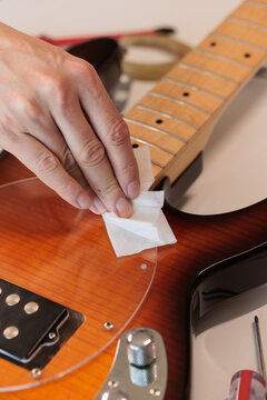 Hands polishing the wooden body of an electric bass guitar