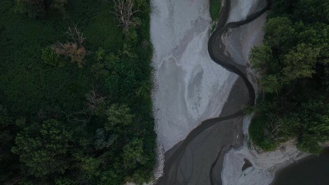 A dry secondary channel of the Po River in Emilia Romagna, Italy, exposes broad alluvial sediments and braided fluvial patterns after prolonged summer drought across Po Valley, top-down drone fly