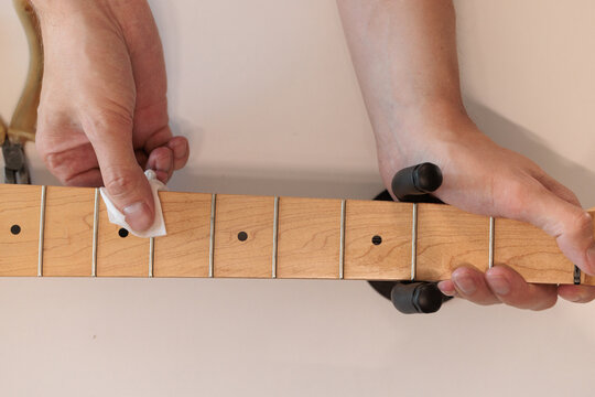 Hands cleaning a maple bass guitar fretboard with a white cloth