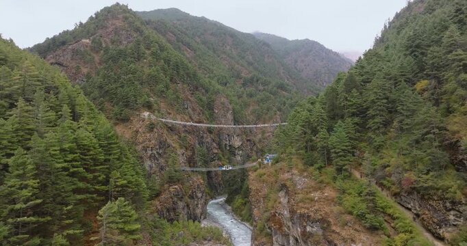Everest region, Nepal, Drone shot of the iconic Hillary Suspension Bridge hanging high across a deep rocky canyon above the rushing white waters of the Dudh Koshi River.
