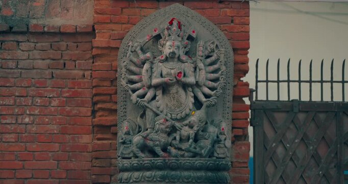 Bhaktapur, Nepal, medium tracking shot of the historic stone relief sculpture of the multi-armed deity Ugra Chandi Durga mounted on a traditional red brick wall in UNESCO Durbar Square.