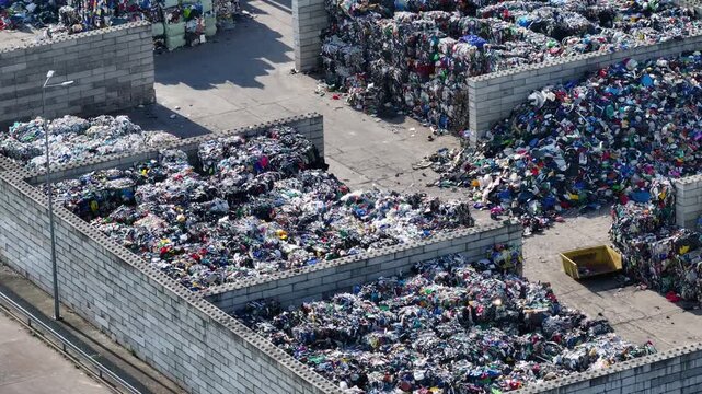 Plastic waste is shown in large piles at a recycling facility. Workers handle materials and sort plastics for further processing. The facility focuses on waste management and recycling.