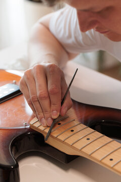 Technician filing frets on an electric bass guitar neck