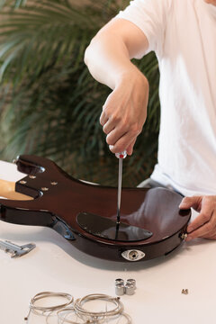 Man unscrewing the electronics cavity cover of a bass guitar