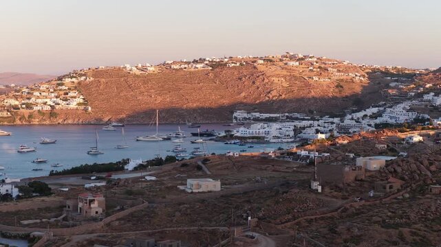 Scenic Mykonos harbour with luxury yachts during golden hour, Greek island landscape showing beach and traditional Cycladic architecture in Aegean Sea