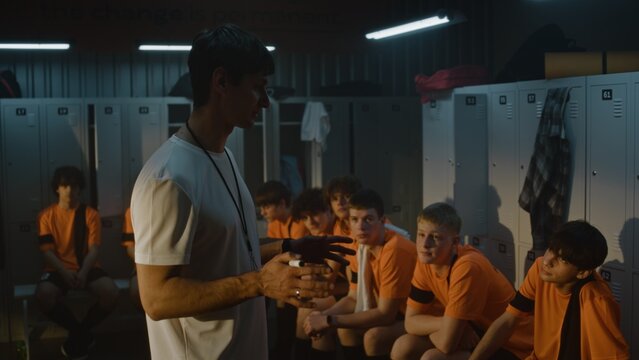 Passionate Male Coach Stands Before Diverse Group of Teenage Football Players in Locker Room. Man Gestures, Giving Motivational Pre Match Instructions and Tactical Advice. Sports Mentorship, Strategy.