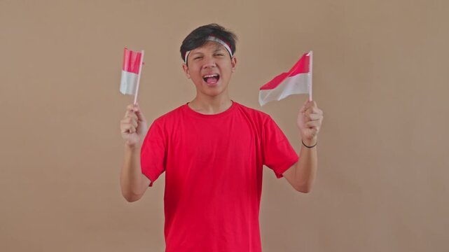Indonesian teenager enthusiastically waving two mini flags to celebrate Independence Day in studio