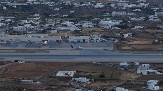 Commercial passenger airliner parked at Mykonos Airport, Greece, panoramic scenery of iconic white architecture and dry landscape during twilight