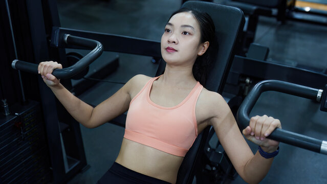 Asian woman using chest press machine in gym for fitness workout