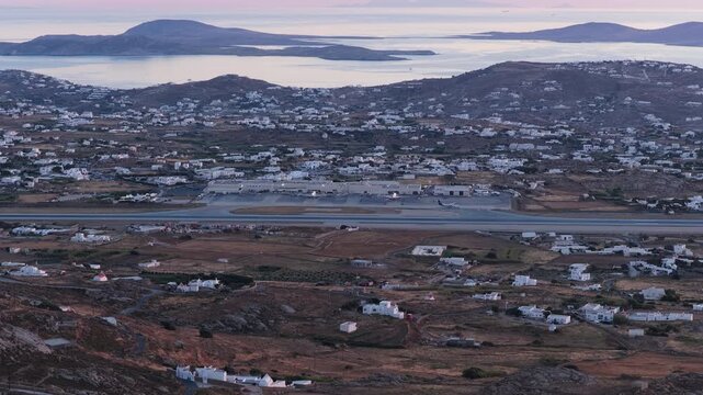 Aircrafts waiting for departure at Mykonos Airport in Greece, Cycladic houses, Aegean Sea, rolling hills of South Aegean islands during twilight