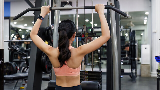 Rear view of Asian woman performing lat pulldown exercise in gym