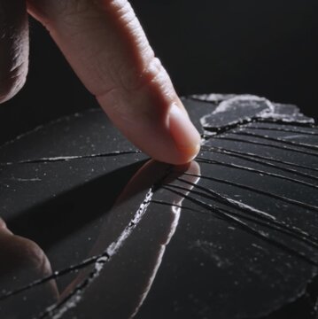 Extreme Close-Up of a Finger Touching a Cracked Volcanic Obsidian Glass Surface