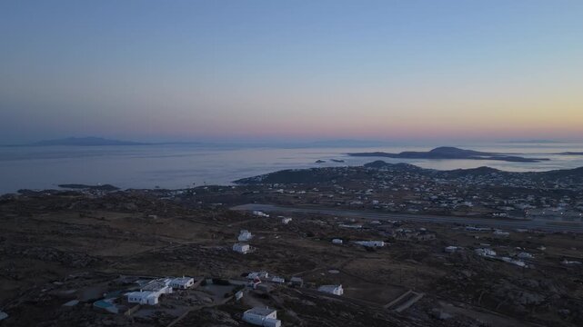 Mykonos Airport and coastline panorama during summer twilight with traditional white houses dotting rocky landscape and Aegean Sea in Greece