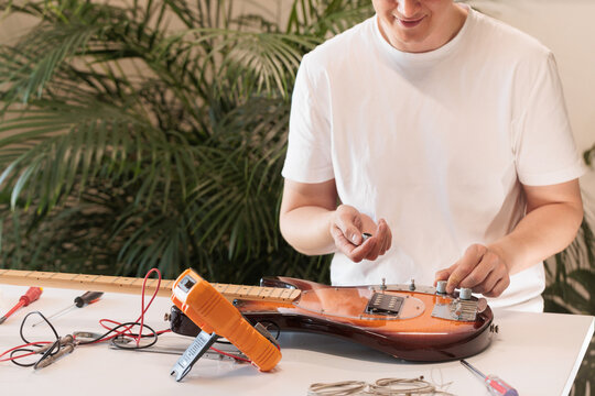 Repairman fitting control knobs to an electric bass guitar body
