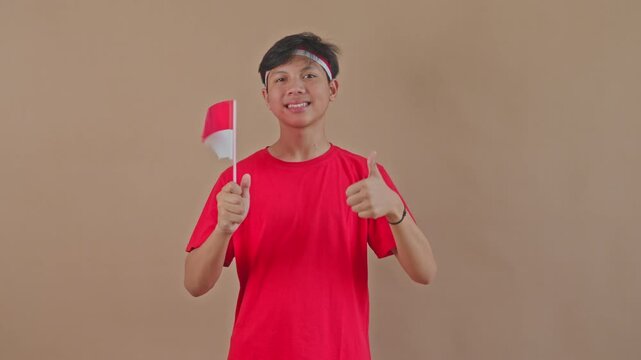 Happy Asian boy showing approval with thumbs up while holding the red and white flag