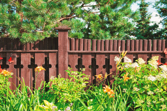 Rustic wooden fence with decorative pattern stands amid lush leaves